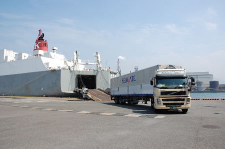 A photo of a truck carrying containers being unloaded from a ship in domestic intermodal transportation.